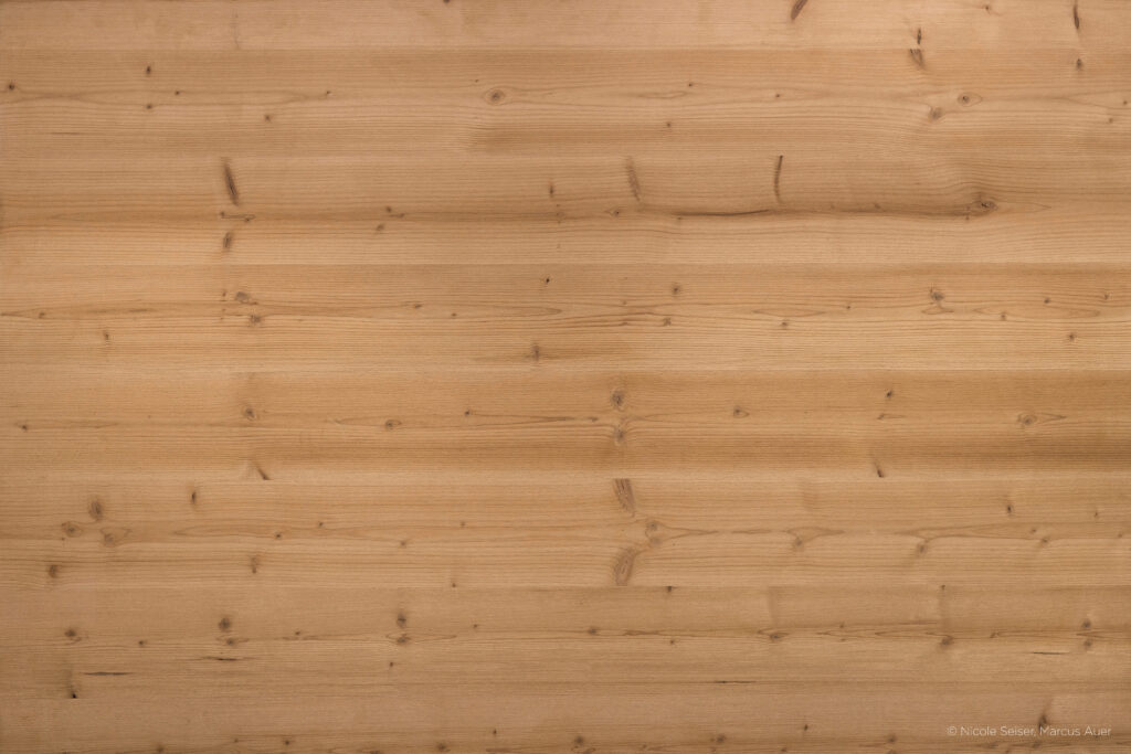Geschliffene Holzoberfläche mit glatter Struktur und feiner, gleichmäßiger Maserung. Wenige, kleine Astlöcher sichtbar. Helle bis mittelbraune Färbung verleiht dem Holz ein ruhiges, natürliches Erscheinungsbild.